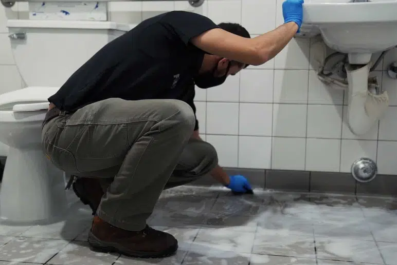 The Business Science of Long-Lasting Restroom Freshness Man kneeling down cleaning a public bathroom floor