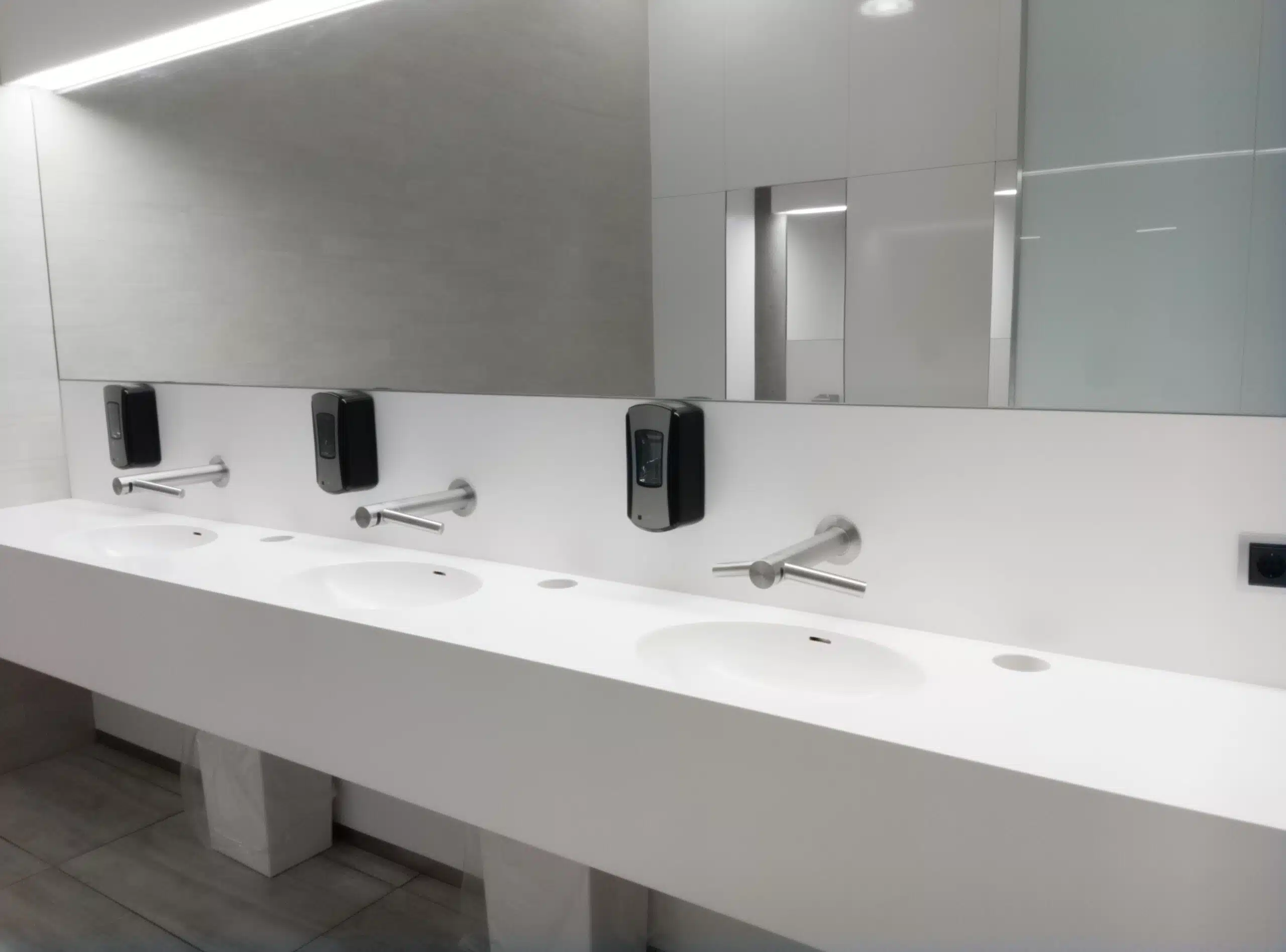 Why Touchless Fixtures Matter for Health, Hygiene & Customer Perception A modern public bathroom with white interior and a mirror with sinks
