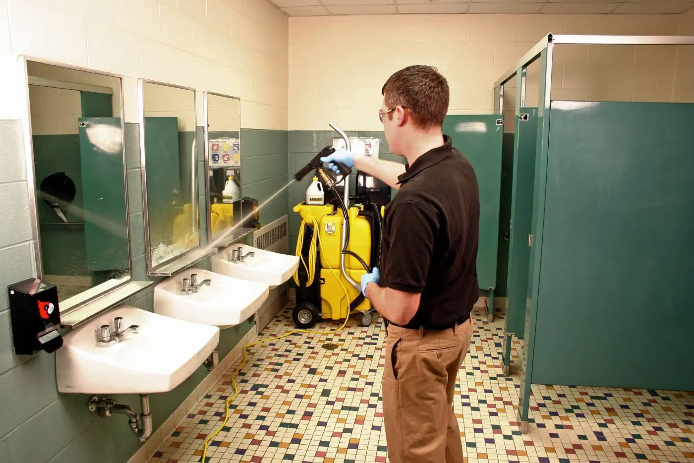 Commercial Restroom Sanitation vs. Basic Janitorial Mopping: What's the Difference? cleaning worker spraying down a restroom and deep cleaning