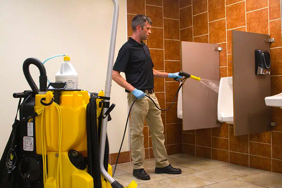 Facility Cold and Flu Prevention: Properly Preparing Manufacturer Restrooms Man spraying down a urinal and cleaning a restroom