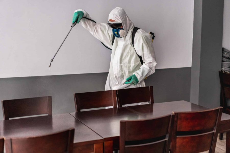 a man in a hazmat suit spraying pest control chemicals and doing a deep clean